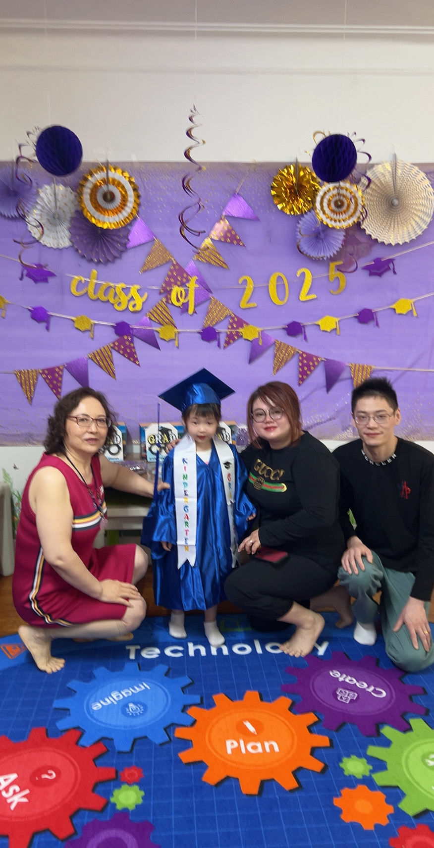 2025届毕业小女孩身穿蓝色学士服与老师及家人在Class of 2025背景墙前合影留念