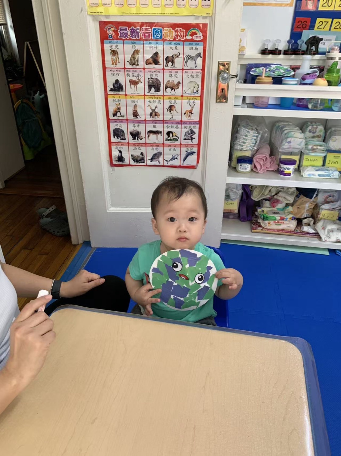 宝宝坐在餐椅旁，背景是中文看图识动物挂图