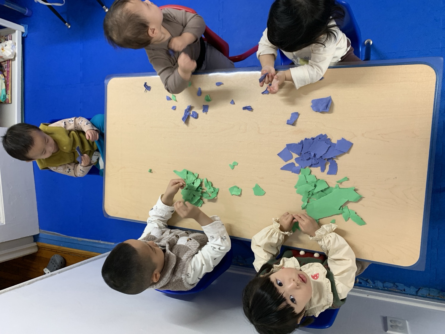 新乐幼儿园小朋友们围坐在桌边一起做撕纸贴画手工活动