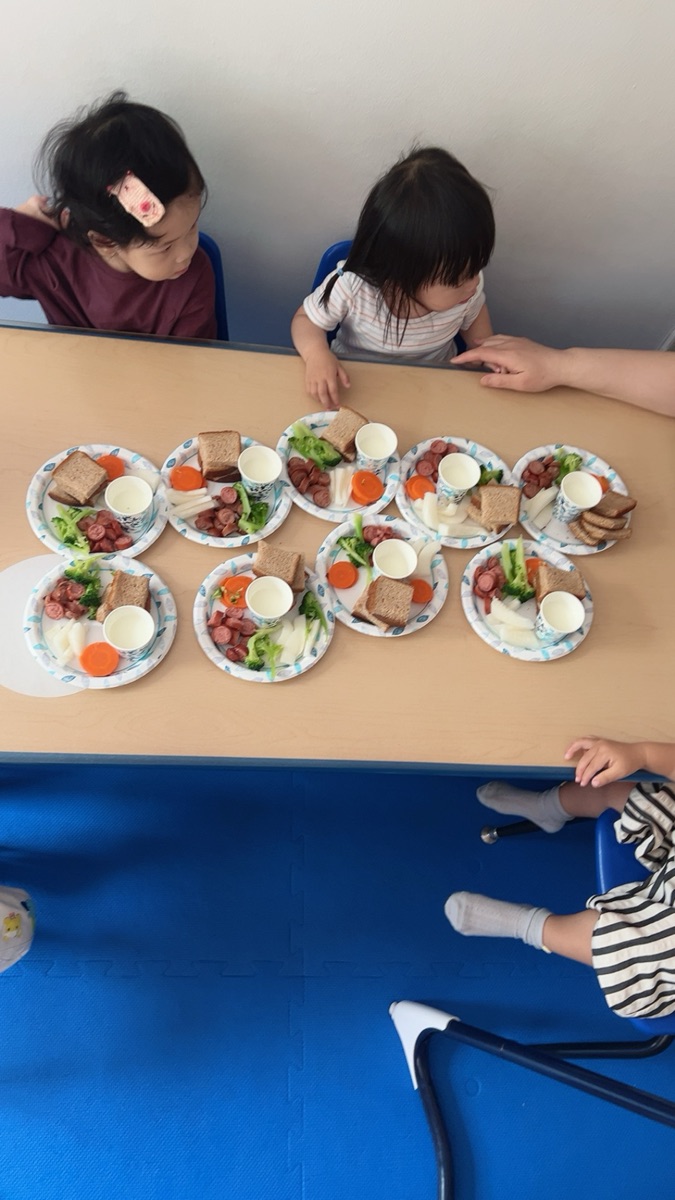 幼儿在教室餐桌前享用吐司、蔬菜与火腿的午餐时间